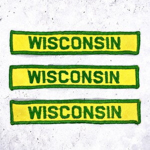 May include: Three rectangular patches with the word "WISCONSIN" embroidered in green on a yellow background. The patches have a green border. The patches are arranged horizontally.