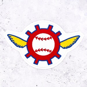 May include: Embroidered patch featuring a baseball design within a red gear, with blue accents and yellow wings. The patch is white with a baseball design in the center, and is likely for a jacket or bag.