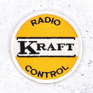 May include: Embroidered patch with a yellow center, white border, and black text. The text reads "RADIO" at the top, "KRAFT" in the center, and "CONTROL" at the bottom. The patch is circular and has a stitched edge.