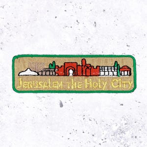 May include: Embroidered patch depicting Jerusalem's skyline, framed by a green border. The design showcases landmarks in red, green, and white, with the text "Jerusalem the Holy City" in gold lettering.