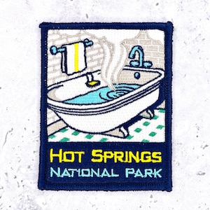 May include: A rectangular embroidered patch featuring a white clawfoot bathtub filled with blue water and rising steam. A towel hangs on a rack above. The bottom section is dark blue with the yellow and light blue text HOT SPRINGS NATIONAL PARK.