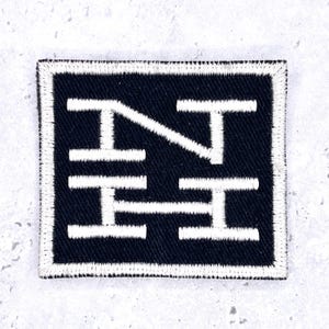 May include: A square embroidered patch featuring a black background with a white border. The design consists of white stitched letters forming the characters N, T, and H, with a diagonal line connecting the N and T, all in a bold, block style.