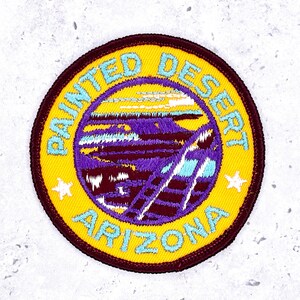 May include: Embroidered patch with the text "PAINTED DESERT ARIZONA" in light blue. The patch has a yellow background with a dark brown border. The center features a purple and blue landscape design with a yellow sky and two white stars.