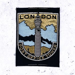 May include: A rectangular embroidered patch featuring a black border and a central depiction of the London Post Office Tower. The design includes gold and light blue threadwork with the text LONDON at the top and POST OFFICE TOWER at the bottom.