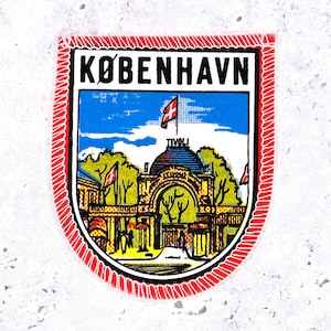 May include: A rectangular embroidered patch with a red stitched border featuring a graphic illustration of the Tivoli Gardens entrance in Copenhagen. The text KØBENHAVN is printed in black at the top, with a blue sky and green trees visible.