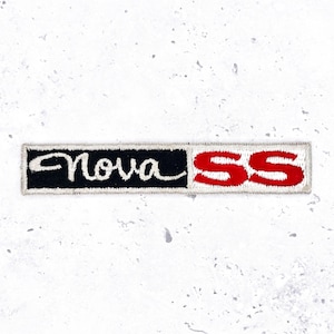Peut inclure: Écusson brodé avec le texte "Nova SS". Le mot "Nova" est en écriture blanche sur fond noir, et "SS" est en lettres rouges. L'écusson a une bordure blanche.