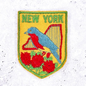 May include: Embroidered patch with a yellow background and a green border. The patch features the text "NEW YORK" above a blue and red bird perched on red flowers. A red harp is also depicted.