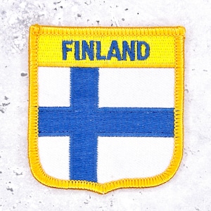 Peut inclure: Un écusson brodé rectangulaire représentant le drapeau de la Finlande avec un fond blanc et une croix bleue. La partie supérieure présente une bordure jaune avec le mot FINLAND brodé en lettres capitales bleues. L'écusson est bordé de jaune.