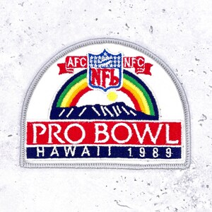May include: A patch featuring the NFL logo, a rainbow, and the words "PRO BOWL HAWAII 1989." The patch has a white background with a gray border. The AFC and NFC logos are also visible.