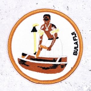 May include: Embroidered patch featuring a Fijian man in a boat, holding a paddle and a staff. The patch has a white background with an orange border and the text "BULA FIJI". The man is depicted in brown and white clothing.