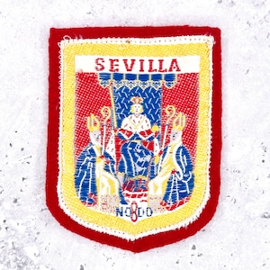 May include: A rectangular embroidered patch featuring a red border and a yellow frame. The center displays the text SEVILLA above a scene with a central figure and two flanking figures in blue and white robes. The text NO8DO appears at the bottom.
