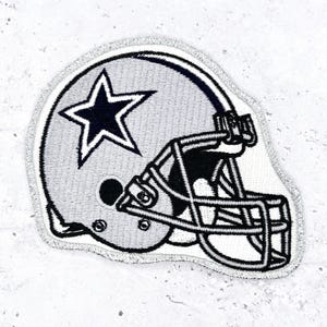 May include: Embroidered patch featuring a football helmet in gray and white, with a navy blue star on the side. The helmet has black detailing and a silver border. This patch is suitable for jackets, bags, or other fabric items.