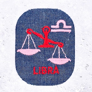 May include: Embroidered denim patch featuring the Libra zodiac symbol. The patch has a dark blue background with a pink scale design and the word "LIBRA" in red. The patch is oval-shaped.