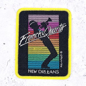 May include: A rectangular embroidered patch with a bright yellow stitched border. The center features a black silhouette of a musician playing a trumpet against a vertical rainbow gradient background. The text reads French Quarter and New Orleans.