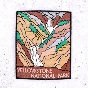 May include: Embroidered patch featuring a colorful landscape of Yellowstone National Park. The design includes waterfalls, mountains, and trees in shades of brown, green, and white. The text "YELLOWSTONE NATIONAL PARK" is at the bottom.