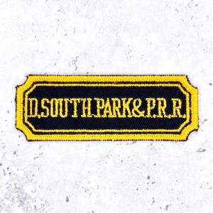 May include: A rectangular embroidered patch with rounded corners featuring a black background and a yellow border. The text D.SOUTH PARK & P.R.R. is stitched in yellow capital letters across the center of the patch in a serif font.