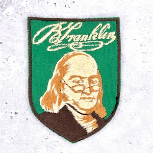 May include: Embroidered patch featuring a portrait of Benjamin Franklin, with the name "B. Franklin" in script above. The patch has a green background, brown border, and uses tan, brown, and white thread.