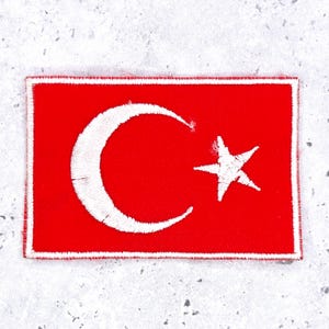 May include: A rectangular embroidered patch featuring a vibrant red background with a white crescent moon and a white five-pointed star centered on the fabric. The patch has a clean white stitched border framing the entire rectangular shape.