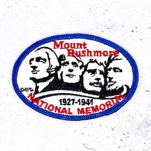 May include: Embroidered patch featuring Mount Rushmore National Memorial. The patch has a blue border and includes the text "Mount Rushmore National Memorial 1927-1941". The image depicts the faces of four U.S. presidents in black and white.