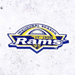 Può includere: Toppa ricamata con il logo dei St. Louis Rams. La toppa ha un bordo bianco con un design blu e giallo. Il testo "INAUGURAL SEASON" è arcuato in alto, con "ST. LOUIS" e "Rams '95" sotto.