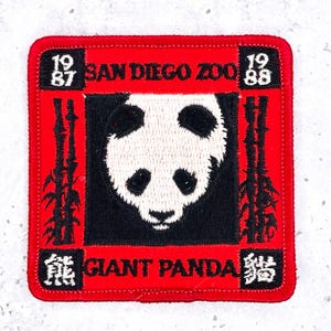 May include: A square embroidered patch with a red border featuring a central black square containing a white and black giant panda face. The text reads SAN DIEGO ZOO, GIANT PANDA, 1987, and 1988. Black bamboo stalks flank the panda, and Chinese characters are in the bottom corners.