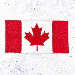May include: Embroidered patch featuring the Canadian flag. The design includes a white center with a red maple leaf, flanked by two red vertical bars. The patch is rectangular and has a stitched border, suitable for application on clothing or accessories.