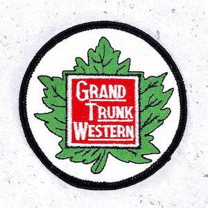Op de afbeelding: Geborduurde patch met een groen esdoornbladontwerp en een rood vierkant in het midden. Het vierkant bevat de woorden "GRAND TRUNK WESTERN" in witte letters. De patch heeft een witte achtergrond en een zwarte rand.