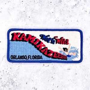 May include: A rectangular embroidered patch with a blue border. It features the red text KAMIKAZEEEEE, the blue text Wet'n Wild, and the black text ORLANDO, FLORIDA. An embroidered figure is shown splashing into blue water on the right side.