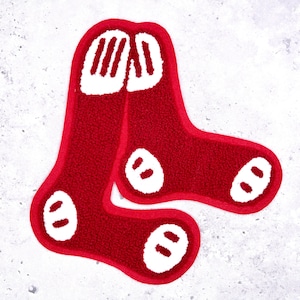 May include: A pair of red and white decorative socks, possibly a rug or mat. The socks are a bright red with white detailing, including the top and three oval shapes on each sock. A fun and striking home decor piece.