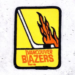 May include: A rectangular patch with a yellow background, black border, and the words "VANCOUVER BLAZERS" in orange. A white hockey stick and orange flames are also featured.