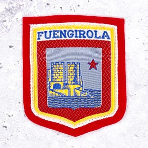 May include: A red, shield-shaped embroidered patch with the word "FUENGIROLA" at the top. The patch features a castle design in yellow and blue, a red star, and a decorative border.