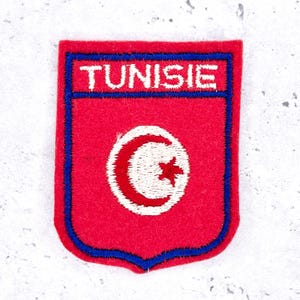 Peut inclure: Écusson brodé rouge et bleu avec le mot "TUNISIE" en blanc. Le patch en forme de bouclier présente un croissant de lune blanc et une étoile rouge, symbolisant la Tunisie.