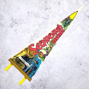 May include: A vintage pennant with the words "Sequoyah Caverns" in red, featuring a colorful illustration of a waterfall, a person, and a building. The pennant has a yellow tip and yellow tabs.
