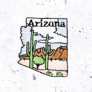 May include: Embroidered patch in the shape of Arizona, featuring the state name in black. The patch depicts a desert landscape with green cacti, brown mountains, and a blue sky. The patch is outlined in black.