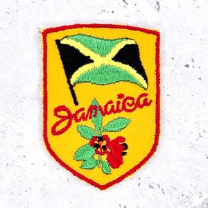 Peut inclure: Écusson brodé avec le drapeau jamaïcain et le mot "Jamaica" en script rouge. L'écusson a un fond jaune avec une bordure rouge et un motif floral avec des fleurs rouges et des feuilles vertes.