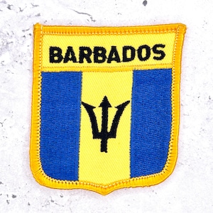 May include: A rectangular embroidered patch featuring the Barbados flag design with a yellow top section displaying the word BARBADOS in black thread. The lower section features a vertical blue, yellow, and blue tricolor with a black trident.