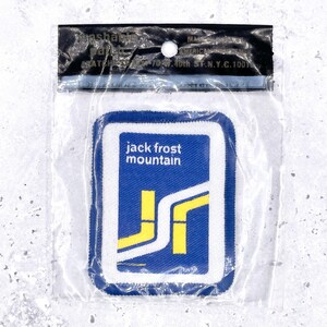 Op de afbeelding: Een blauwe, witte en gele patch met de woorden "jack frost mountain" in witte tekst. De patch heeft een witte rand en een geel en wit grafisch ontwerp. De patch zit in een doorzichtige plastic zak.