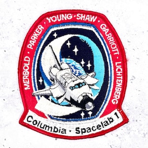 May include: Embroidered patch featuring the Columbia Spacelab 1 mission. The patch has a red border with the names of the crew members. The central design shows a space shuttle, a crescent moon, stars, and a blue and white Earth.