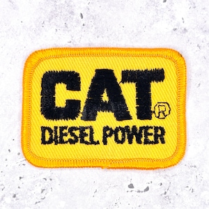 May include: A rectangular embroidered patch featuring a bright yellow background with a thick yellow stitched border. The text CAT is embroidered in large black letters, with the word DIESEL POWER in smaller black letters underneath.