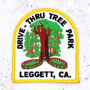 Pode incluir: Um emblema bordado com borda amarela e fundo branco. Apresenta uma árvore castanha com uma abertura para passagem, folhagem verde e uma cerca castanha. O texto diz DRIVE-THRU TREE PARK e LEGGETT, CA. em letras pretas.