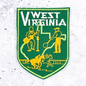 May include: A shield-shaped embroidered patch in green with a white border. The text WEST VIRGINIA is stitched in white at the top. Below, yellow thread depicts a person playing a guitar, a person holding a tool, and a horse with a rider.