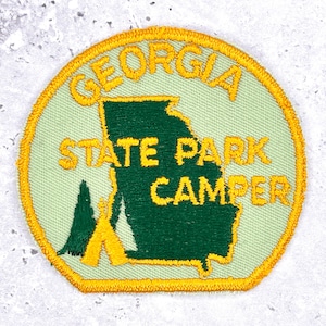 May include: Embroidered patch with a light green background and a yellow border. The patch features the outline of the state of Georgia in dark green, with the words "GEORGIA STATE PARK CAMPER" in yellow.