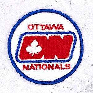 May include: A circular patch with a white background, a blue border, and the words "OTTAWA NATIONALS" in red. The center features a red and blue design with a white maple leaf.