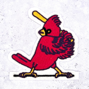 May include: Embroidered patch featuring a red cardinal bird holding a yellow baseball bat. The bird has black and purple detailing and yellow legs. The patch is outlined in white and is on a light gray background.