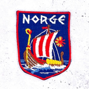 May include: Embroidered patch with a shield shape, featuring a Viking ship with red and white striped sails, yellow accents, and the word "NORGE" in white letters on a blue background. The patch has a red border.