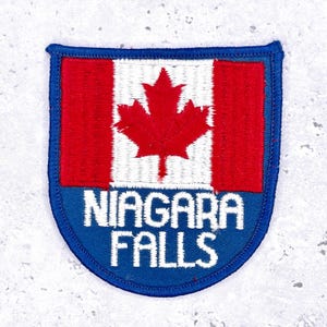 May include: Embroidered patch featuring the Canadian flag with a red maple leaf on a white background, above a blue banner with the text "NIAGARA FALLS" in white. The patch has a blue border.