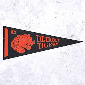 May include: Black pennant with orange detailing, featuring the Detroit Tigers logo. The pennant displays a roaring tiger graphic and the words "DETROIT TIGERS" in orange. A vintage sports collectible.