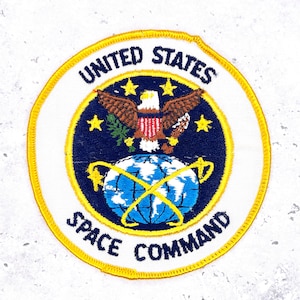 May include: Embroidered patch featuring the United States Space Command emblem. The circular patch has a white background with a gold border. The design includes a bald eagle, stars, and a globe, with the text "UNITED STATES SPACE COMMAND".