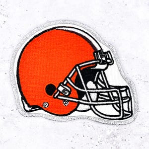 以下が含まれることがあります： アメフトのヘルメットの刺繍パッチ。ヘルメットはオレンジ色で、黒いフェイスマスクと白い縁取りがあります。パッチは、生地にアイロンをかけるか縫い付けるように設計されています。