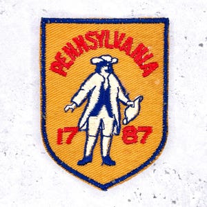 May include: A yellow and blue Pennsylvania patch with a shield shape. The patch features the word "PENNSYLVANIA" in red, a blue and white figure, and the numbers "1787" in red.